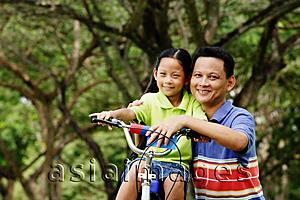 Asia Images Group - Girl on bicycle, father next to her, both looking at camera