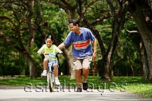 Asia Images Group - Father and daughter in park, daughter cycling, father running alongside her