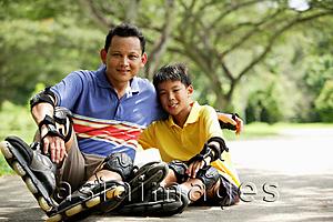 Asia Images Group - Father and son, sitting in park, wearing roller blades