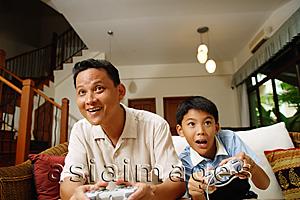 Asia Images Group - Father and son, sitting on sofa, playing with video games