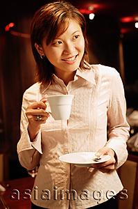 Asia Images Group - Woman holding cup and saucer, looking away, smiling