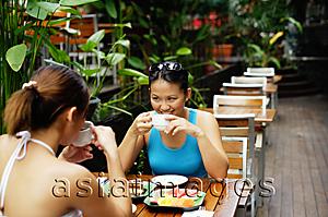 Asia Images Group - Two women sitting at table, having coffee and fruits