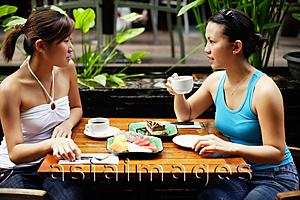 Asia Images Group - Two women sitting at table, having coffee and fruits