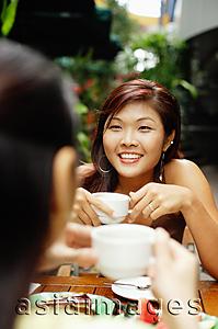 Asia Images Group - Two women facing each other holding coffee cups.