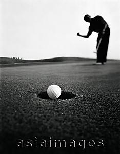 Asia Images Group - Asian golfer putting ball in hole