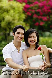 Asia Images Group - Couple sitting on park bench, looking at camera, woman holding rose