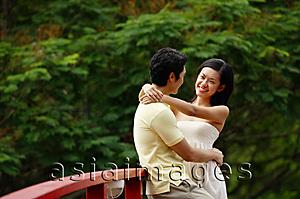 Asia Images Group - Couple standing face to face on bridge, woman with arms around mans neck