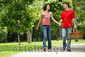 Asia Images Group - Couple walking in park, looking at each other, man carrying picnic basket