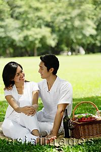 Asia Images Group - Couple sitting with picnic basket, smiling at each other
