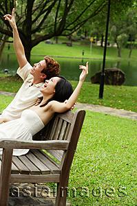 Asia Images Group - Couple sitting on park bench, looking up