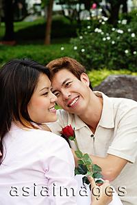 Asia Images Group - Couple sitting on park bench, woman holding a rose, looking away