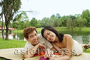 Asia Images Group - Couple lying on mat in park, looking at camera