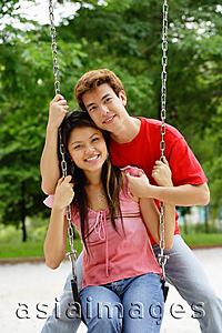 Asia Images Group - Couple in playground, woman sitting on swing, man behind her, smiling at camera