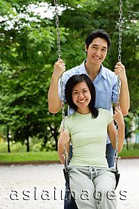 Asia Images Group - Woman sitting on swing, man behind her, smiling at camera