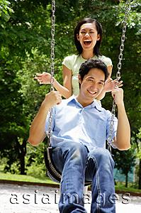 Asia Images Group - Man sitting on swing, woman standing behind him, laughing