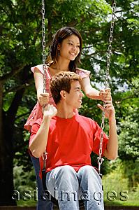 Asia Images Group - Man sitting on swing, woman standing behind him