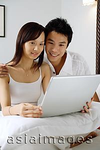 Asia Images Group - Couple sitting on bed, using laptop