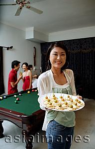 Asia Images Group - Woman holding tray of appetizers, smiling at camera, people in the background