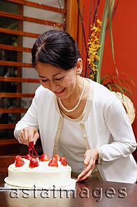 Asia Images Group - Mature woman cutting birthday cake, smiling