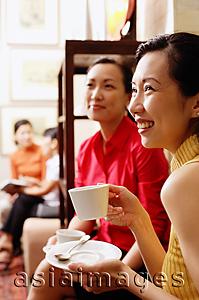 Asia Images Group - Women smiling, holding cups and saucers, looking away