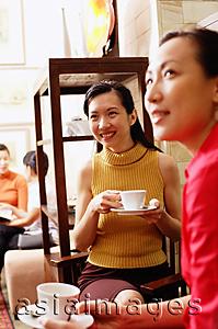 Asia Images Group - Women sitting, holding cups and saucers, looking away