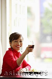 Asia Images Group - Woman sitting at table, raising drink towards camera