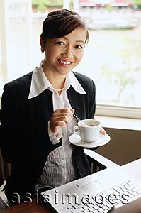 Asia Images Group - Businesswoman holding cup and saucer, smiling at camera