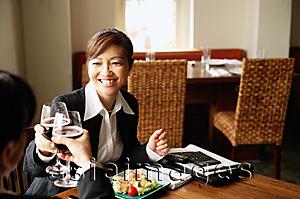 Asia Images Group - Two businesswomen sitting at table, toasting with drinks