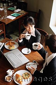 Asia Images Group - Two businesswomen at cafe, drinking coffee, laptop on table
