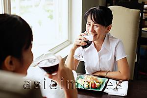 Asia Images Group - Two women at restaurant, sitting face to face, drinking wine, food on the table