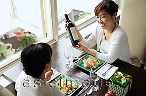 Asia Images Group - Two women in restaurant having lunch, one woman holding bottle of wine