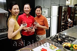 Asia Images Group - Three women in kitchen, holding wine glasses, smiling at camera
