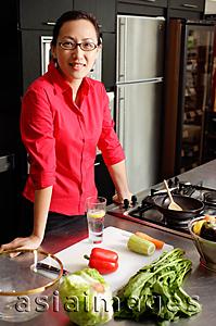 Asia Images Group - Woman in kitchen, leaning on counter, looking at camera