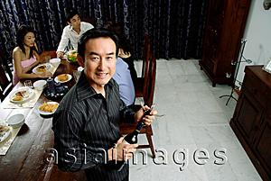 Asia Images Group - Man holding wine bottle, smiling at camera, people in the background