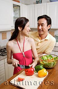 Asia Images Group - Couple in kitchen, woman chopping vegetables, looking over shoulder, smiling at man