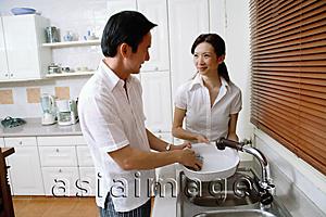 Asia Images Group - Couple in kitchen, man washing dishes, woman next to him