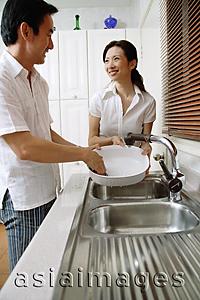 Asia Images Group - Couple in kitchen, man washing dishes, woman standing next to him, smiling