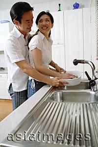 Asia Images Group - Couple in kitchen, woman washing dishes, man standing behind her