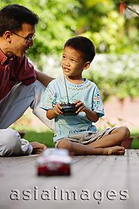 Asia Images Group - Son playing with remote control toy car, father next to him