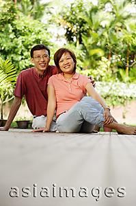 Asia Images Group - Couple sitting on floor, side by side, looking at camera