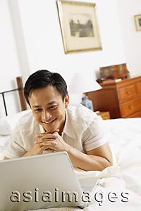 Asia Images Group - Man in bedroom, looking at laptop, hands clasped, under chin