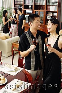Asia Images Group - Couple in dining room, holding wine glasses, people in the background