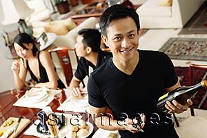 Asia Images Group - Man looking at camera, holding wine bottle, people in the background