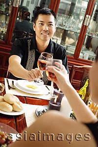 Asia Images Group - Couple toasting wine glasses across dining table, over the shoulder view