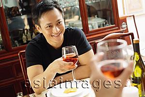 Asia Images Group - Man holding wine glass, smiling at person across from him