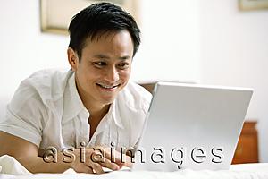 Asia Images Group - Man in bedroom, using laptop