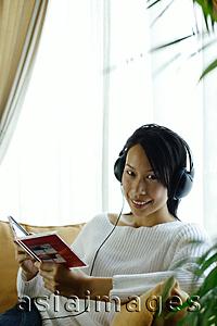 Asia Images Group - Woman sitting on sofa, wearing headphones, looking at camera