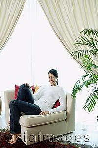Asia Images Group - Woman in living room, sitting on sofa, smiling at camera