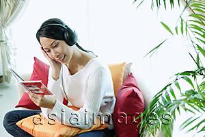Asia Images Group - Woman sitting on sofa, wearing headphones