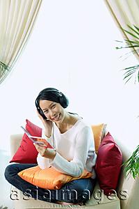 Asia Images Group - Woman sitting on sofa, wearing headphones, smiling at camera, portrait